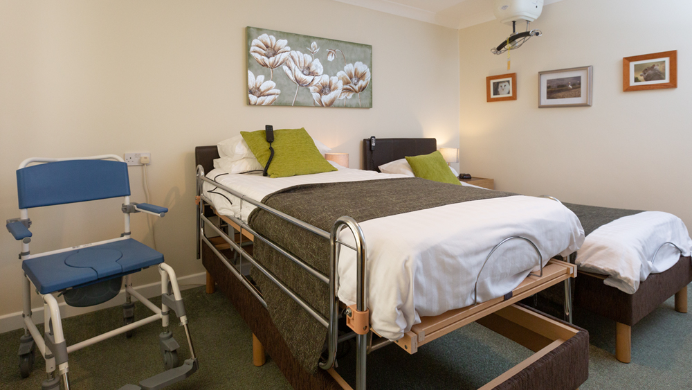 This photo shows the height adjustable bed with a wheeled shower chair and the ceiling hoist